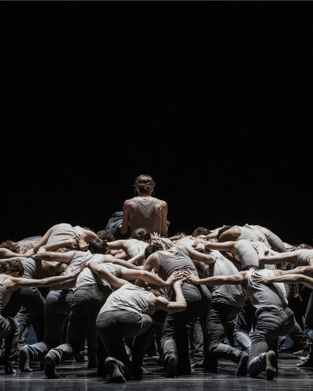 en gruppe dansere bøyer seg mot scenegulvet, en danser står i midten med ryggen til