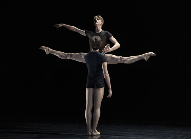 to mannlige dansere, den ene i splitthopp, den andre med ryggen mot oss