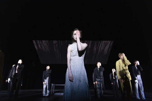 mange dansere på scenen, en kvinne i lys kjole står i forgrunnen