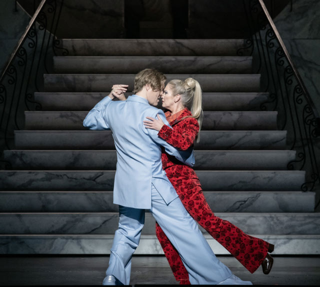 en mann i lyseblå dress danser med dame med lyst hår og rød dress